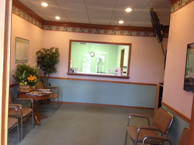 waiting room with chairs on either side and front desk window at back